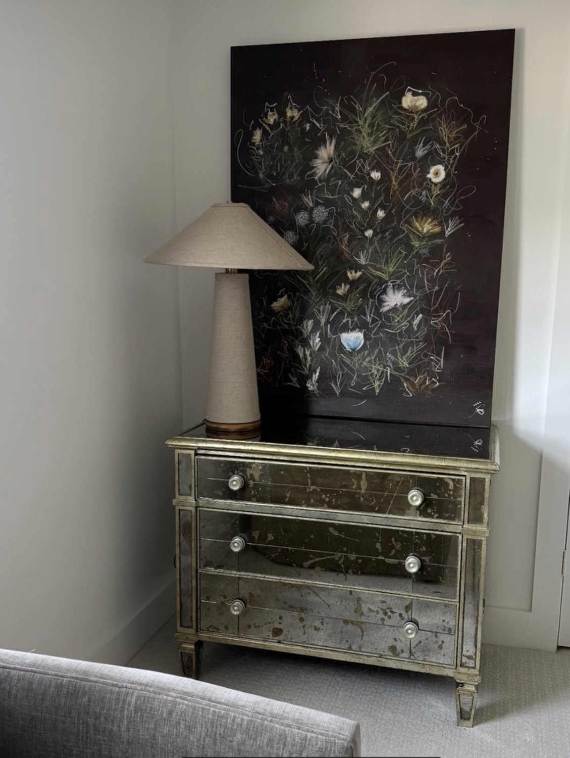 A large dark floral canvas resting above a mirrored chest in a client's room