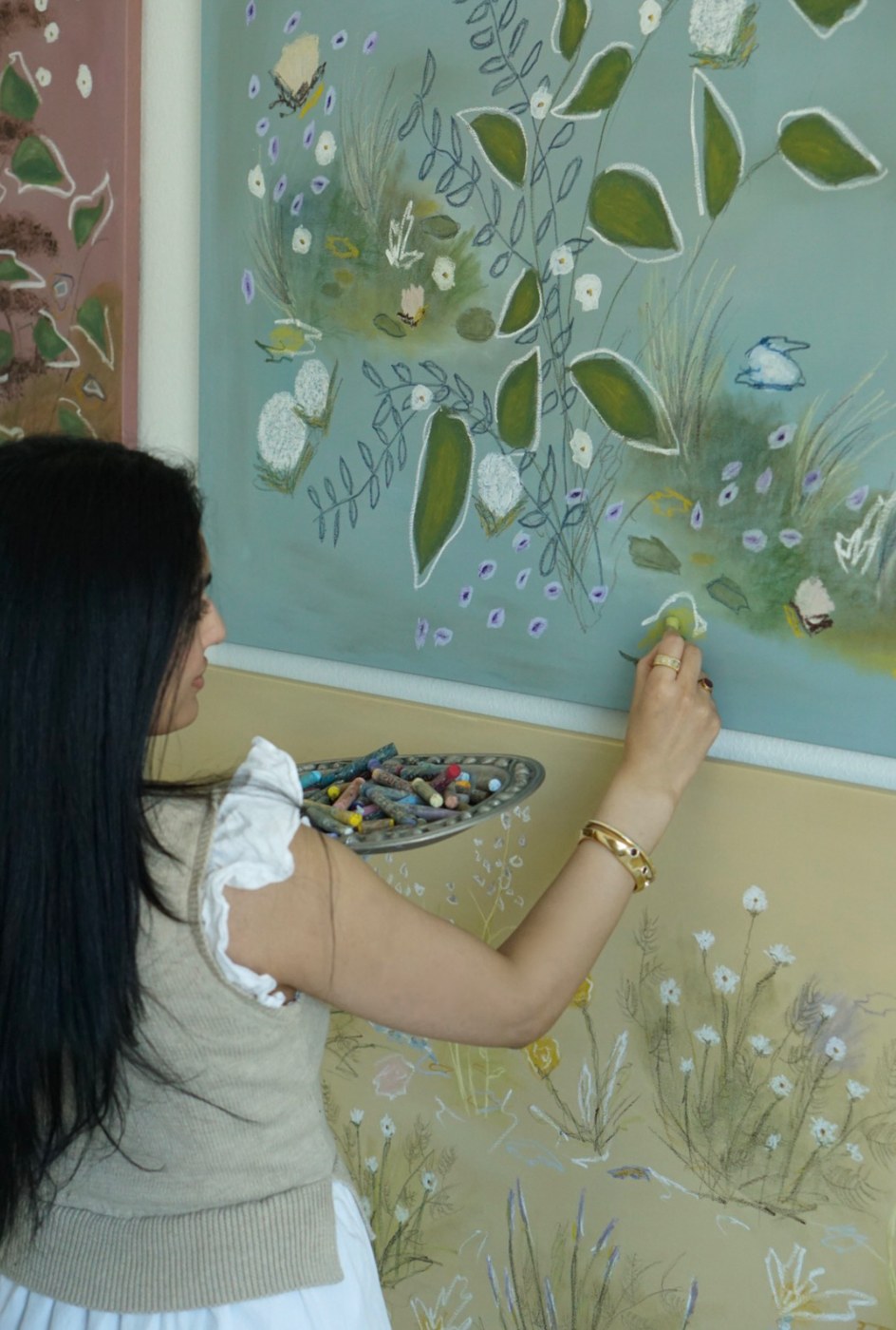 Salma at work on a canvas, a dish of oil pastels in one hand